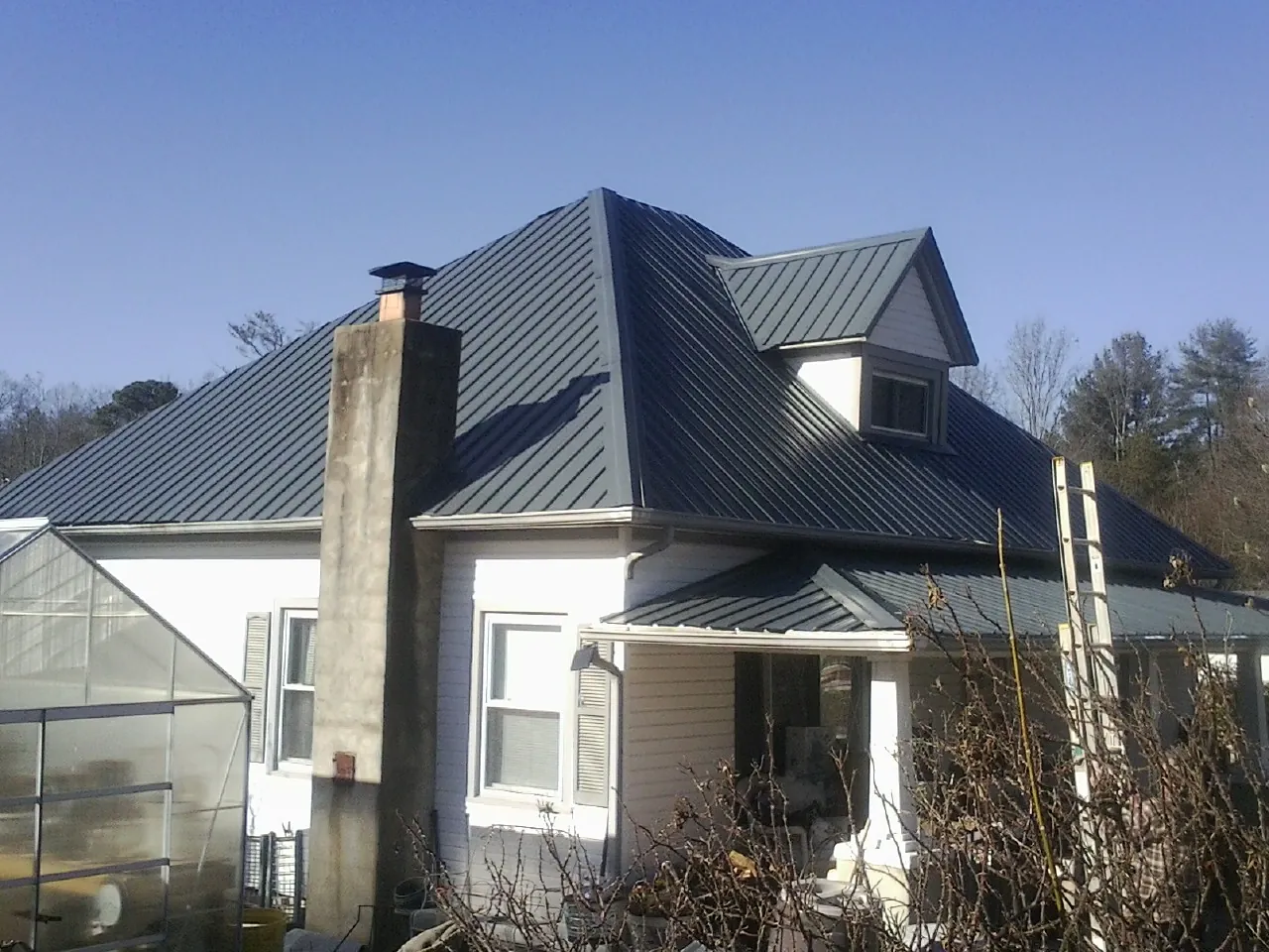 Dark blue standing seam metal roof on a white farmhouse with dormer — Slate & Tile Roof Repair by Roofing Brothers in Stewart