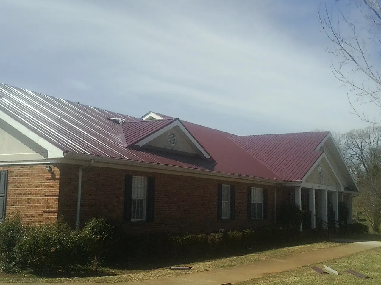 Red metal roof with gabled entries on a long brick building, from a Hail Damage Roof Repair job in Stewart