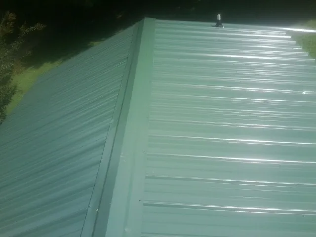 New green metal panels meeting at the ridge of a roof — Flat Roof Repair work by our crew in Stewart